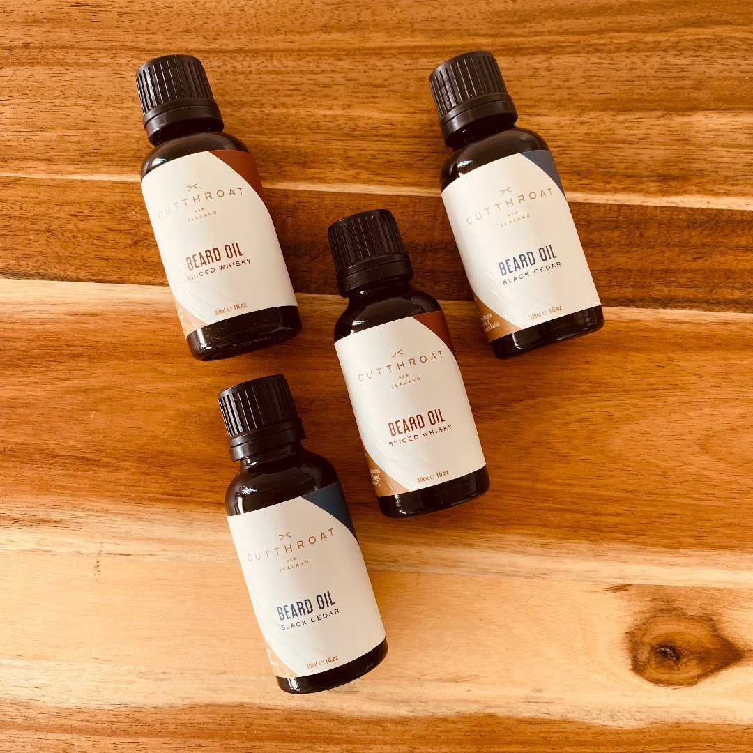 Handmade Black Cedar Beard Oil and Spiced Whisky Beard Oil in recyclable amber glass bottles with black dripolator caps, crafted with natural ingredients like Jojoba and Grape Seed oils. The Black Cedar Beard Oil features a cedarwood and patchouli fragrance, while the Spiced Whisky Beard Oil offers warm notes of whiskey, bay rum, and tobacco.