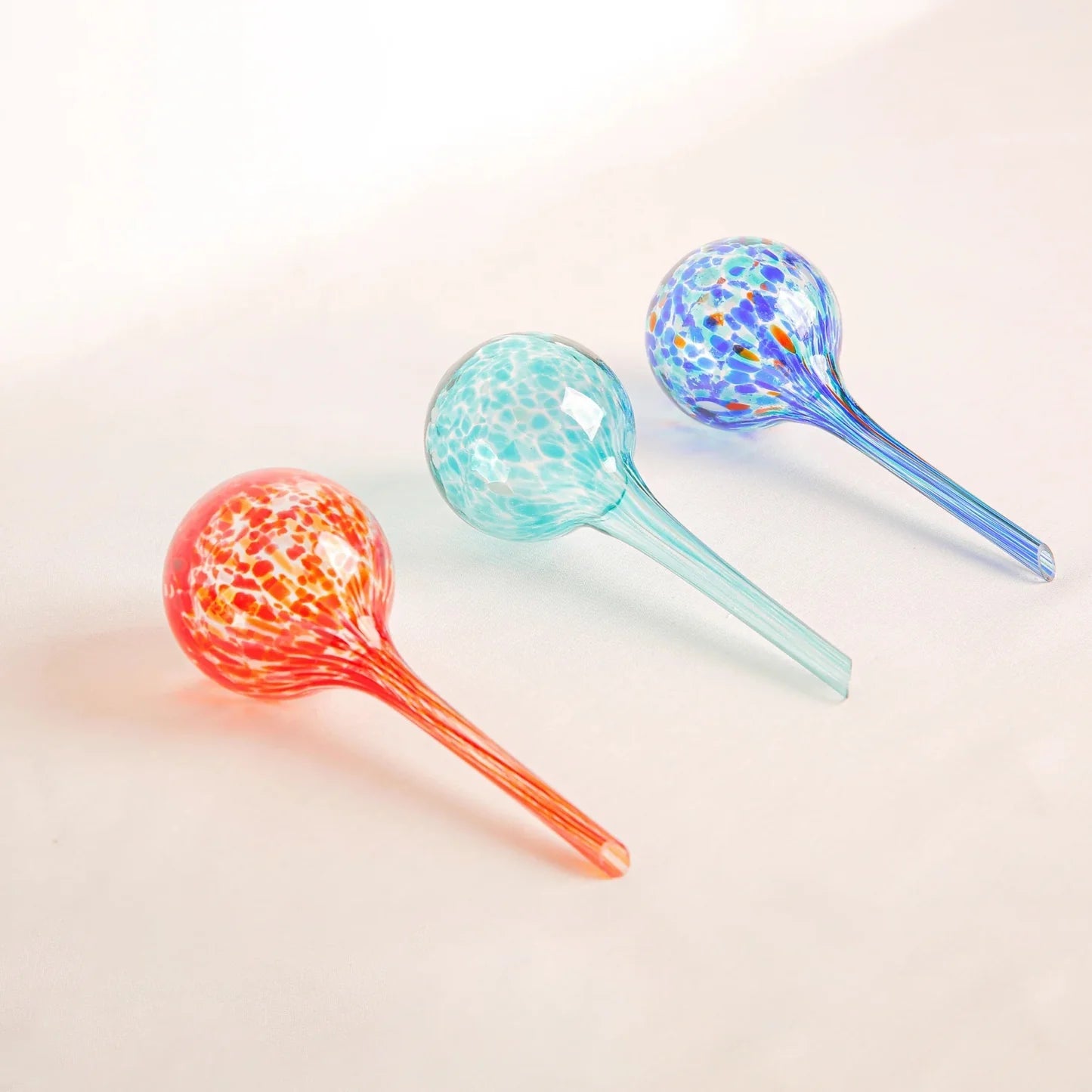 Set of three hand-blown glass plant watering globes – Fire in red-orange-yellow, Aqua in turquoise-green, and Blue in deep blue tones – decorative and functional for indoor and outdoor plants.