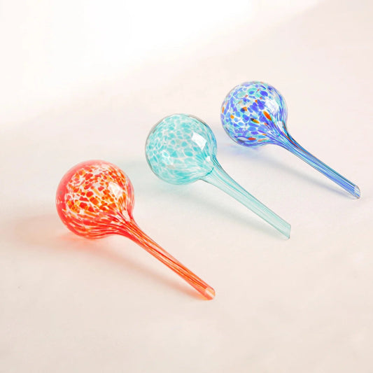 Set of three hand-blown glass plant watering globes – Fire in red-orange-yellow, Aqua in turquoise-green, and Blue in deep blue tones – decorative and functional for indoor and outdoor plants.