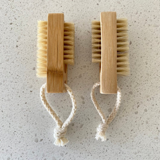 Wooden nail brush with natural bristles in use, gently cleaning beneath nails with warm water and soap.